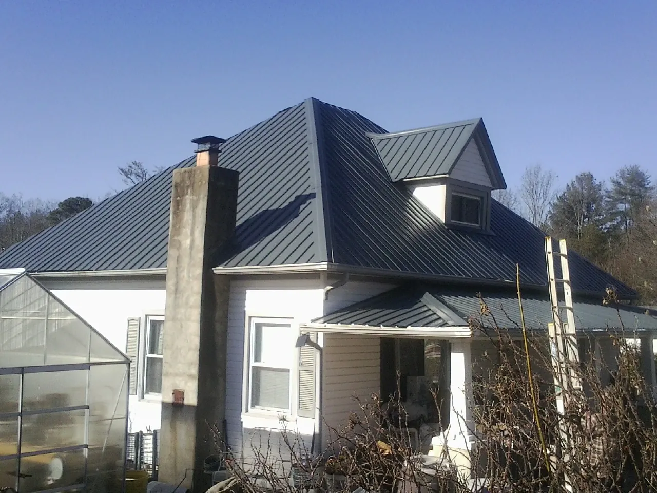 Dark blue standing seam metal roof on a white farmhouse with dormer — Slate & Tile Roof Repair by Roofing Brothers in Minco