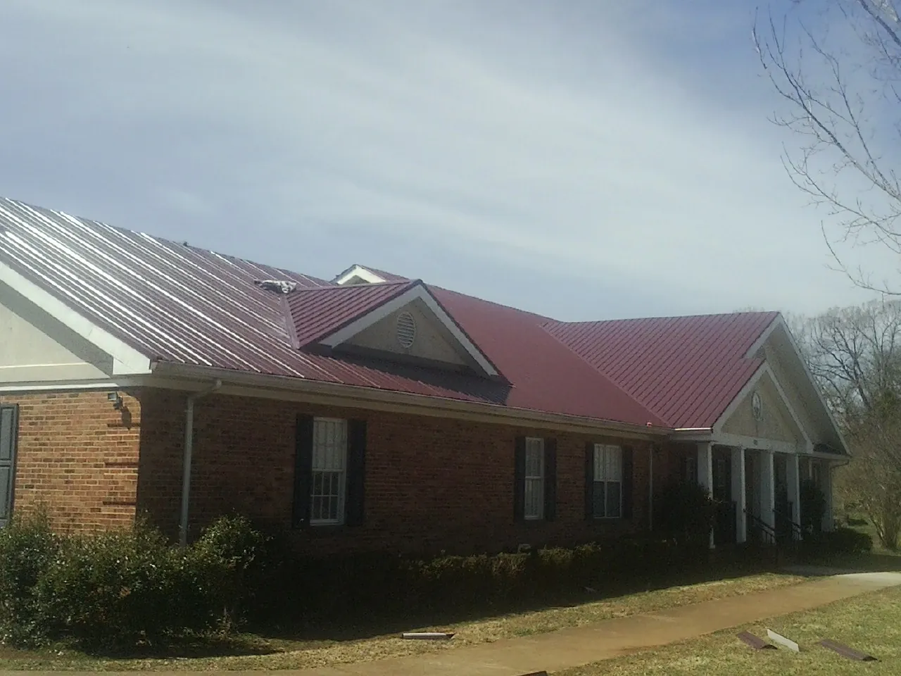 Red metal roof with gabled entries on a long brick building, from a Hail Damage Roof Repair job in Minco
