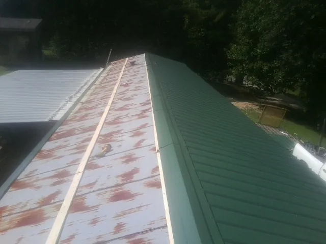 Old rusted panels beside newly installed green metal roofing — Wind Damage Roof Repair by Roofing Brothers in Minco