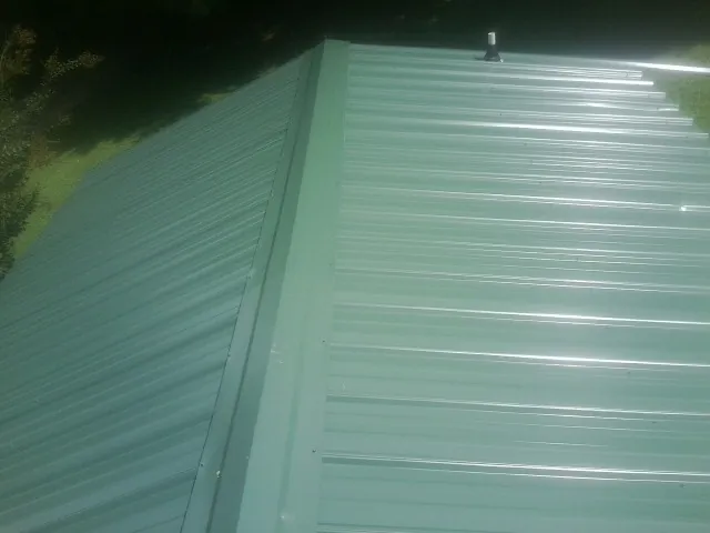 New green metal panels meeting at the ridge of a roof — Flat Roof Repair work by our crew in Minco