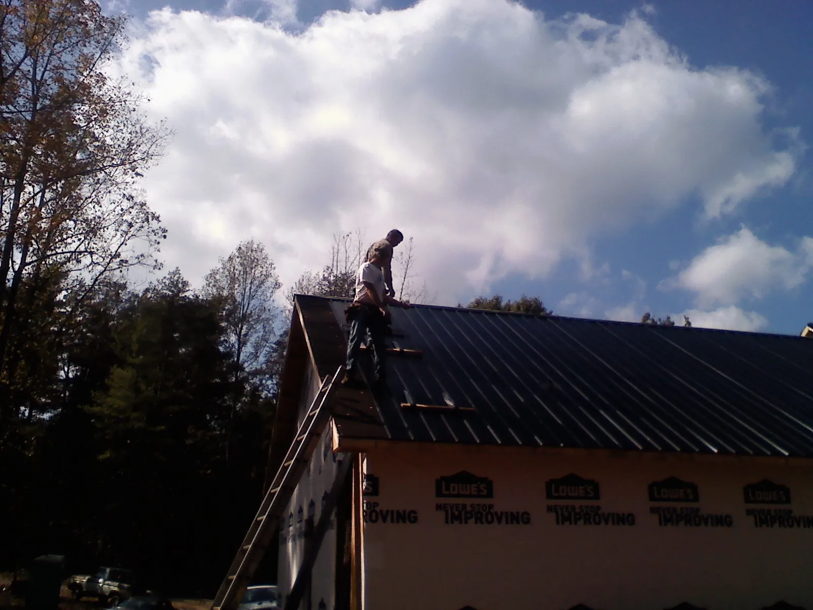 Roofer fastening dark metal panels high against a cloudy sky, from a Roof Inspection job in Minco