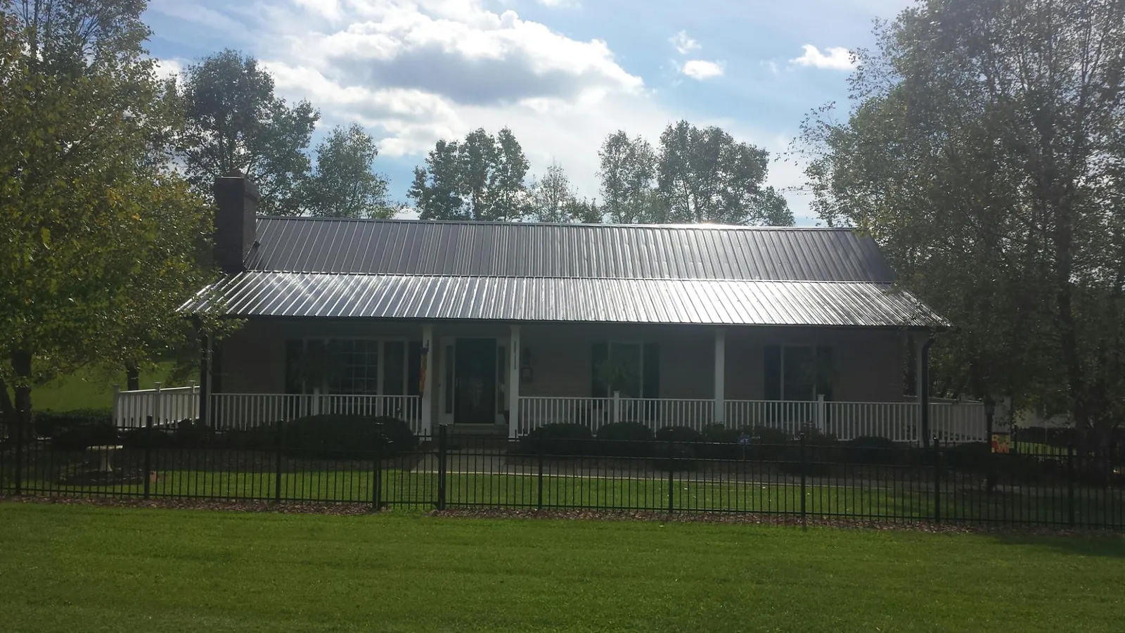 Gray metal roof on a brick ranch with a full width front porch — Gutter Guard Installation work by our crew in Minco