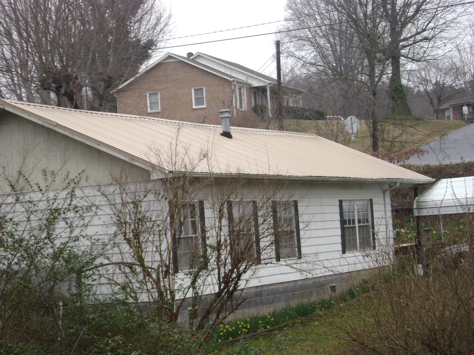 Tan metal roof on a white sided house set into a hillside — Commercial Roofing by Roofing Brothers in Minco