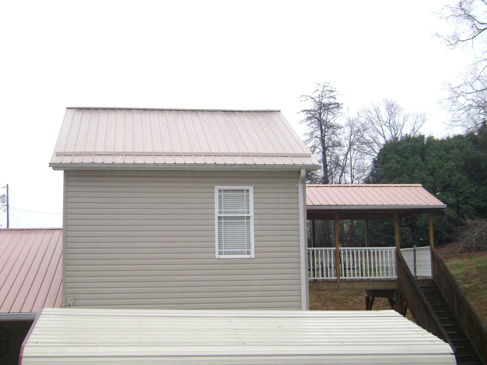 Tan metal roofs on a two story addition and attached porch, from a Roof Replacement job in Minco